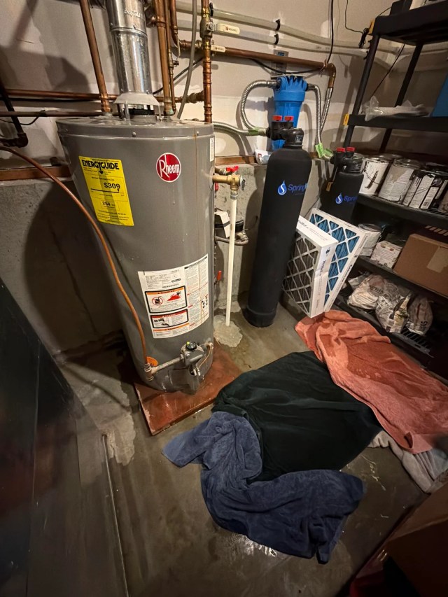 Wet towels on the floor below a water heater.