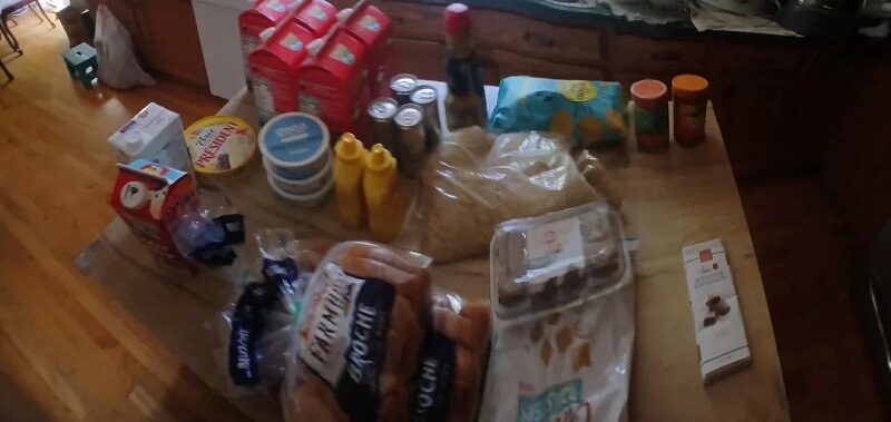 A person holds a shopping basket filled with groceries in a busy store.