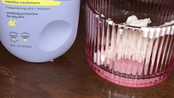 A bottle of vanilla cashmere lotion beside a pink ribbed glass container with cream inside.