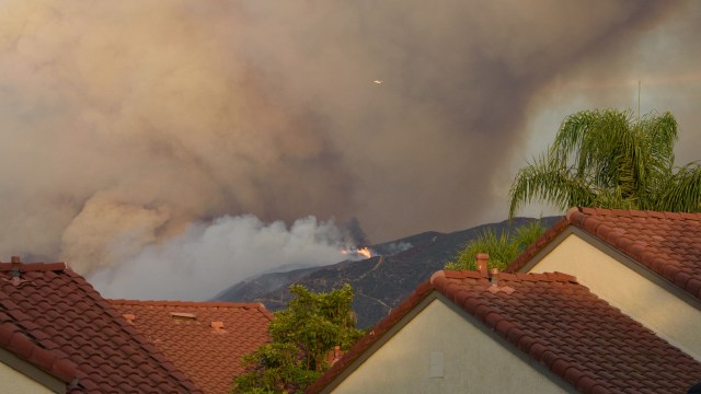 A smoky sky looms over suburban rooftops as a wildfire burns in the distant hills.