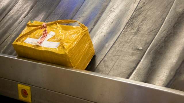 A yellow package with a checked ribbon sits on a baggage carousel in an airport.