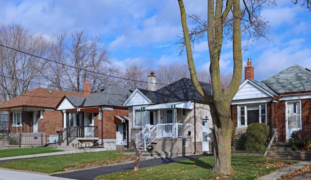 A row of residential homes with varying roof styles, set against a clear blue sky and bare trees.