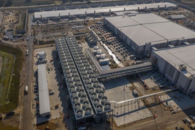 An aerial view of a large data center facility with cooling towers and construction work in progress.