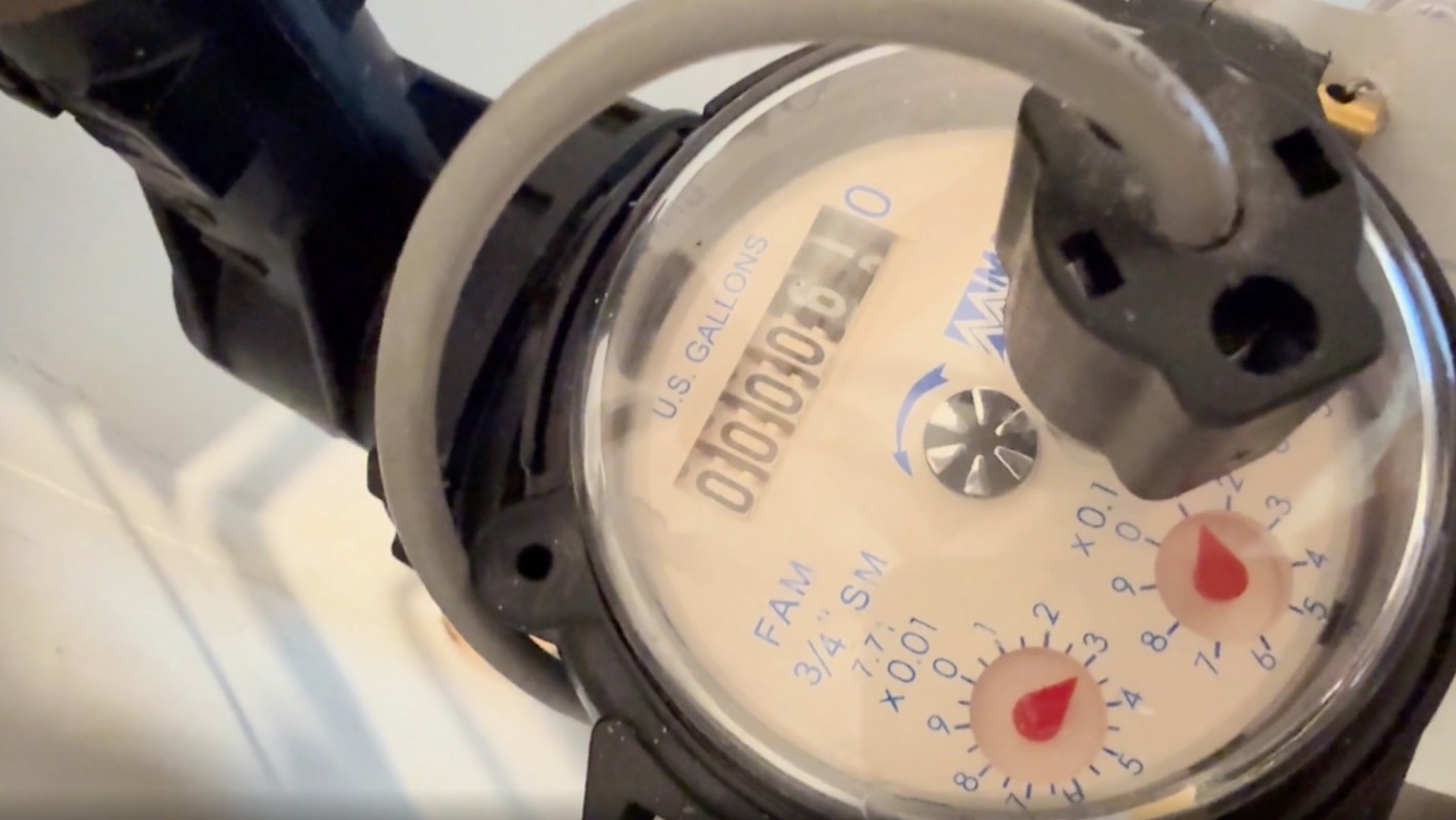 A close-up of a water meter displaying usage in gallons with red dials for precise measurement.