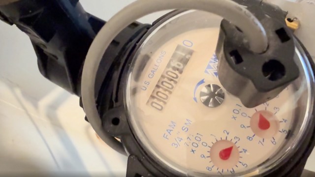 A close-up of a water meter displaying usage in gallons with red dials for precise measurement.