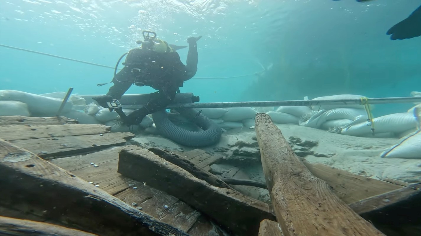 An underwater scene showing a diver working among wooden debris and sandbags on the ocean floor.