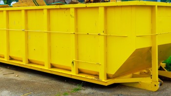 A large yellow dumpster filled with debris, parked on a gravel surface.