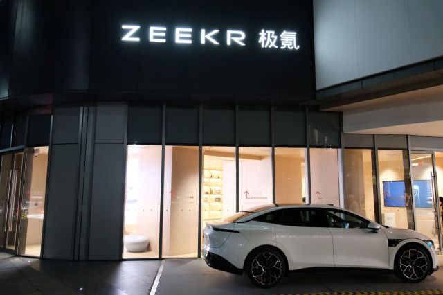 A white electric car parked outside a ZEEKR storefront at night.
