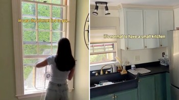 A person with long hair removes a fan from a window while showcasing a small kitchen on the other side.
