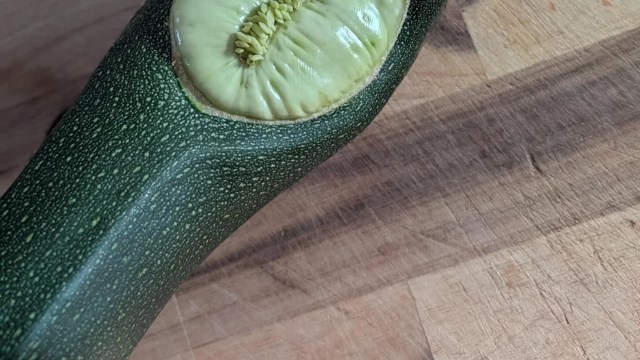 A close-up of a sliced zucchini revealing its pale interior and seeds on a wooden cutting board.