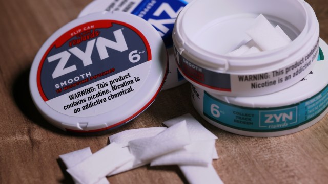 Several containers of ZYN nicotine pouches are displayed with some opened, revealing the pouches on a wooden surface.