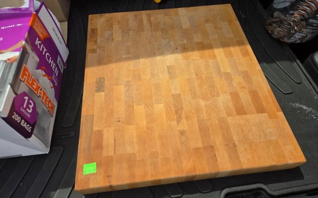 A wooden cutting board on a black surface next to a box of kitchen trash bags.