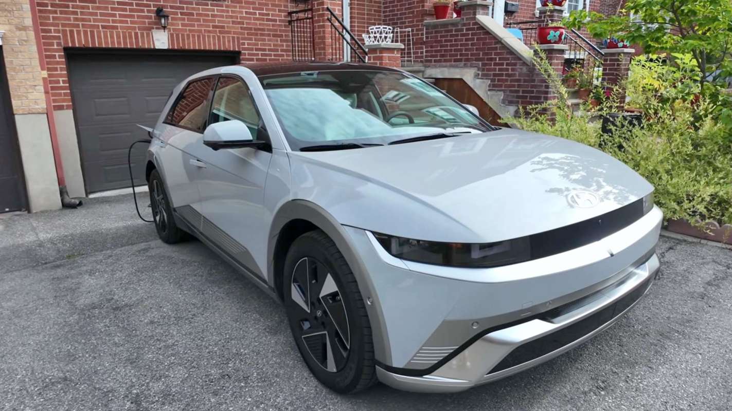 A silver electric vehicle parked on a driveway next to a brick building.