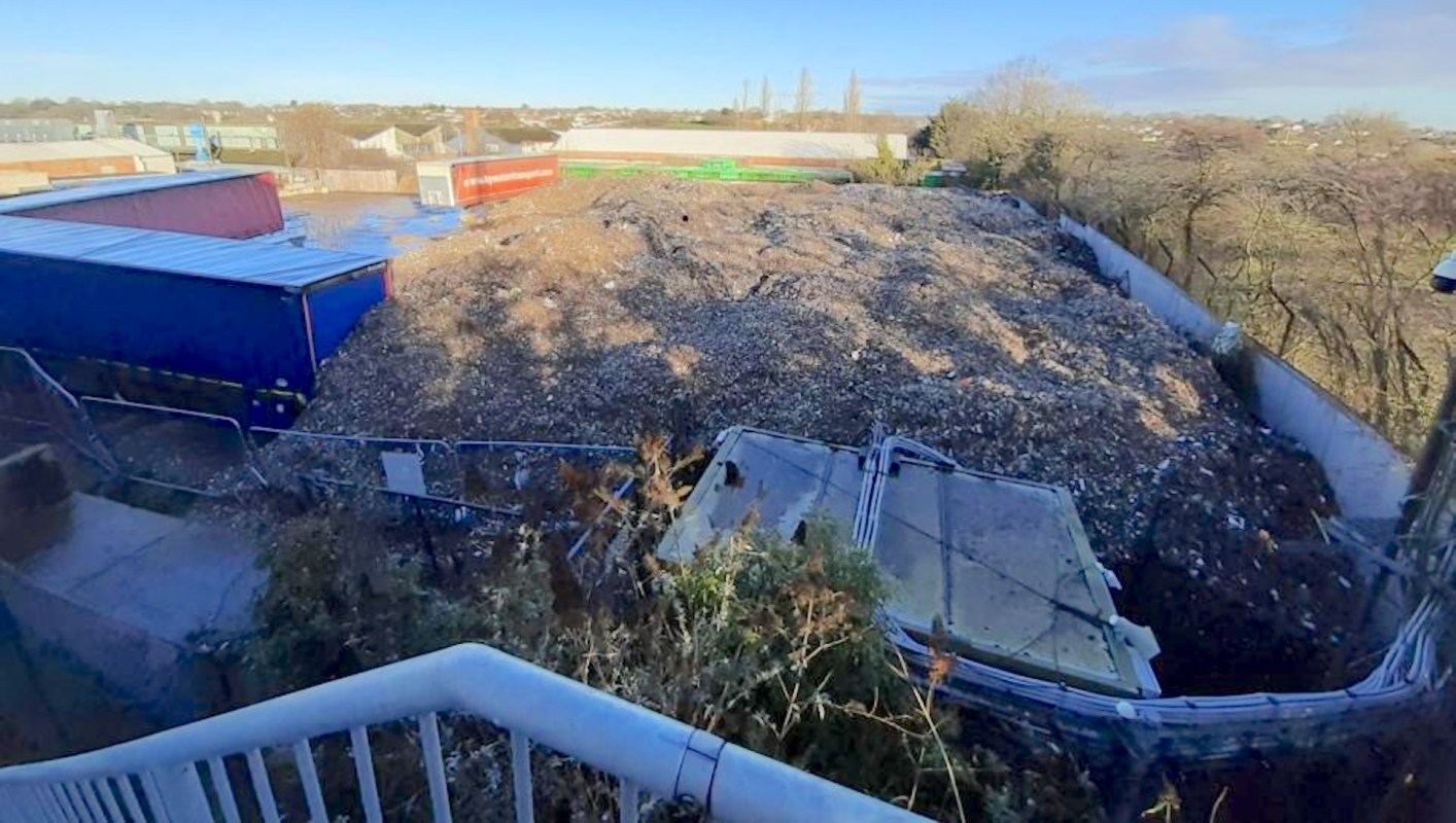 A large pile of debris and waste near industrial buildings with a clear sky in the background.