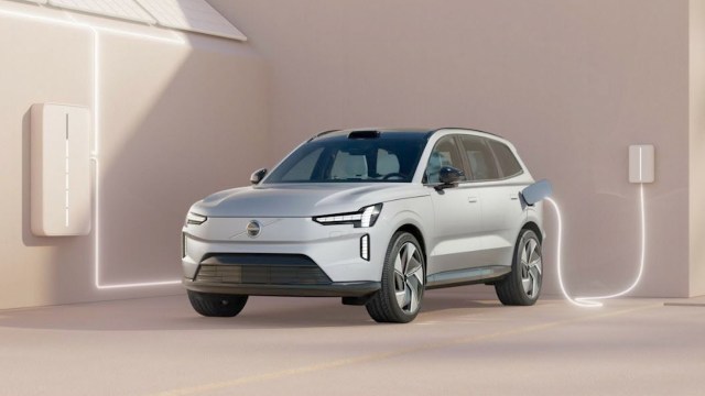 An electric vehicle charging next to a wall-mounted charger with solar panels above.