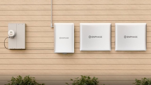 Enphase energy storage system with three white battery units and a meter on a wooden wall.