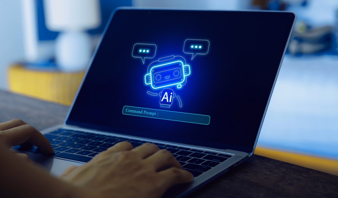 A hand types on a laptop displaying a glowing robot and a command prompt.