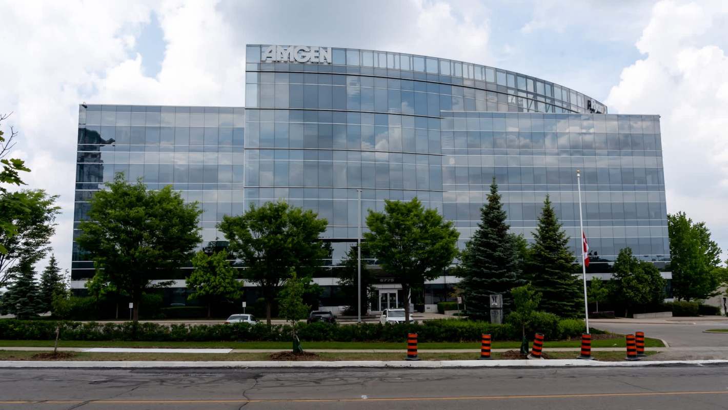 An Amgen office building with large glass windows and greenery in the foreground.