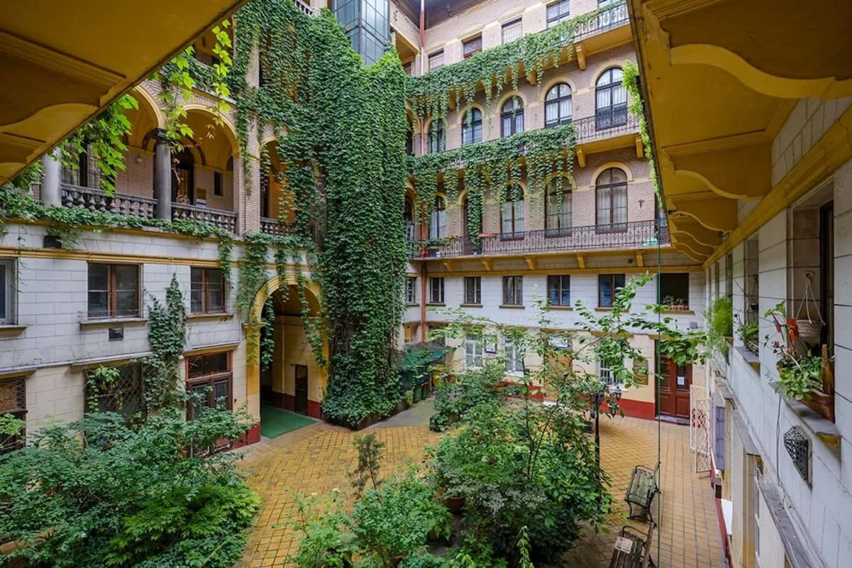 A courtyard surrounded by buildings covered in greenery and featuring various plants and benches.