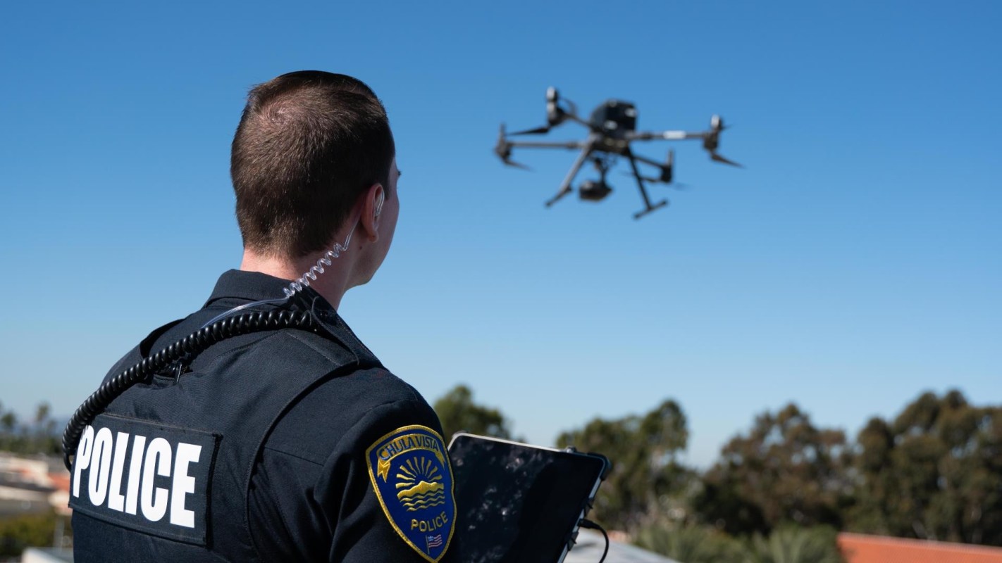 A police officer operates a drone outdoors with a clear blue sky in the background.
