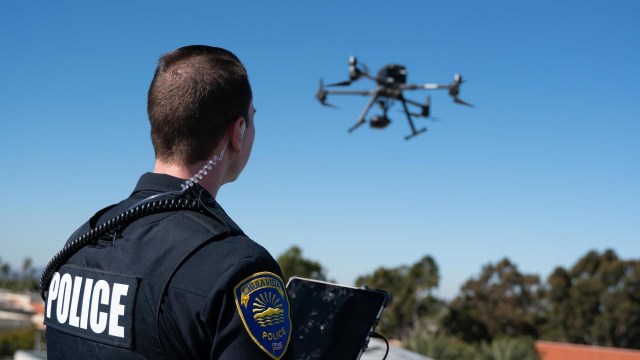 A police officer operates a drone outdoors with a clear blue sky in the background.