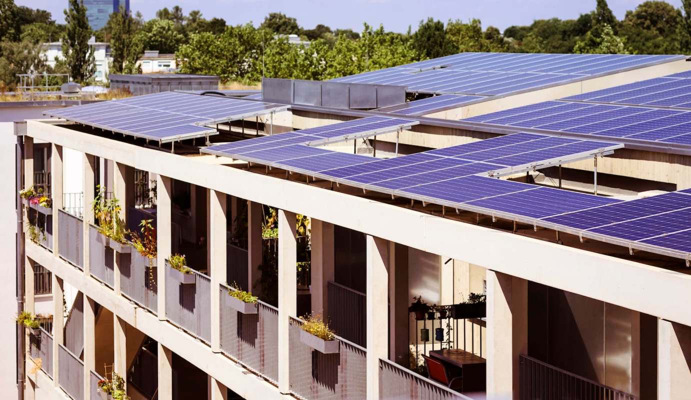 Solar panels installed on the roof of a modern apartment building with greenery on the balconies.