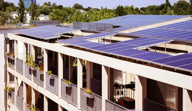 Solar panels installed on the roof of a modern apartment building with greenery on the balconies.