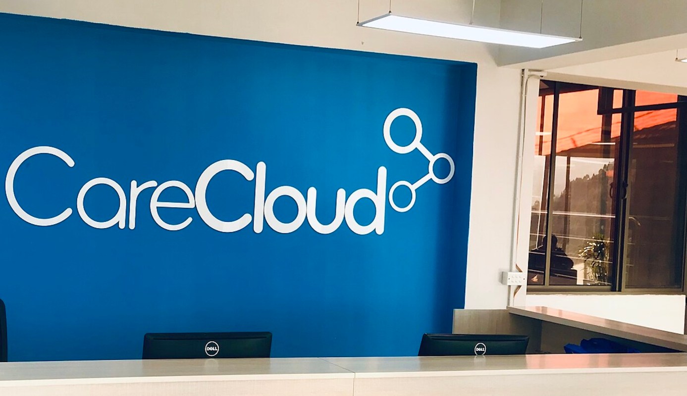A reception area with a blue wall featuring the CareCloud logo and two Dell monitors on a desk.