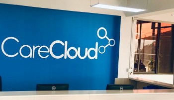 A reception area with a blue wall featuring the CareCloud logo and two Dell monitors on a desk.