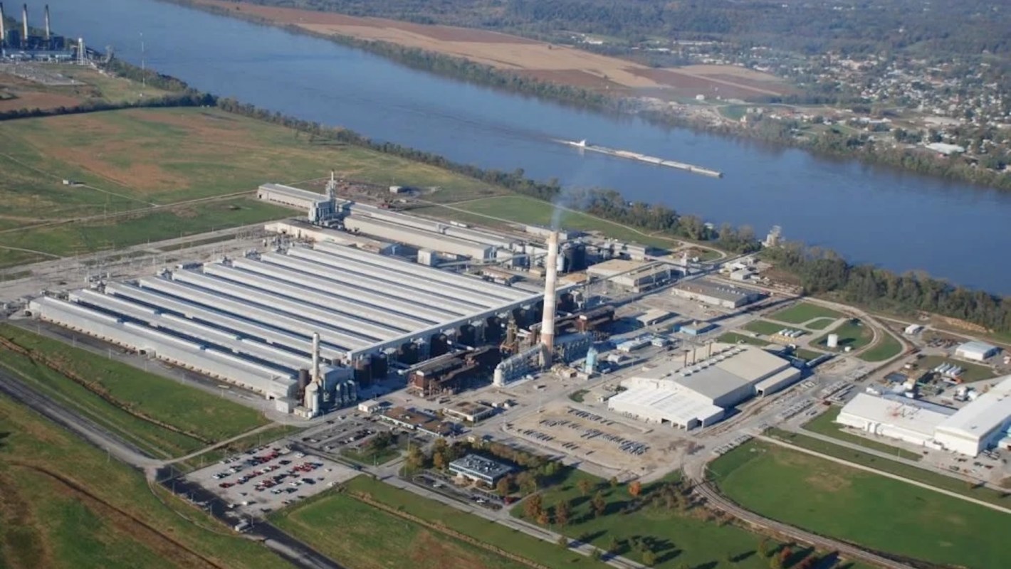 An industrial facility near a river with multiple buildings and smokestacks.