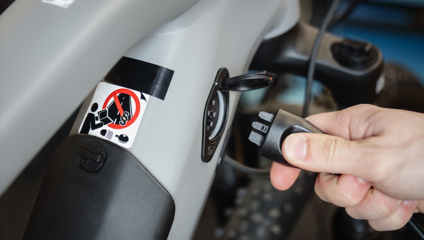 A hand plugging in a connector to the charging port of an electric bike.