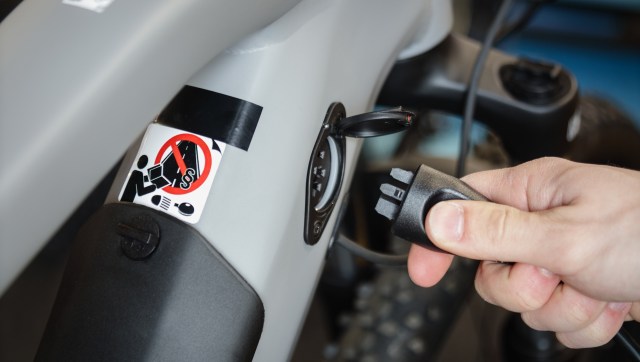 A hand plugging in a connector to the charging port of an electric bike.
