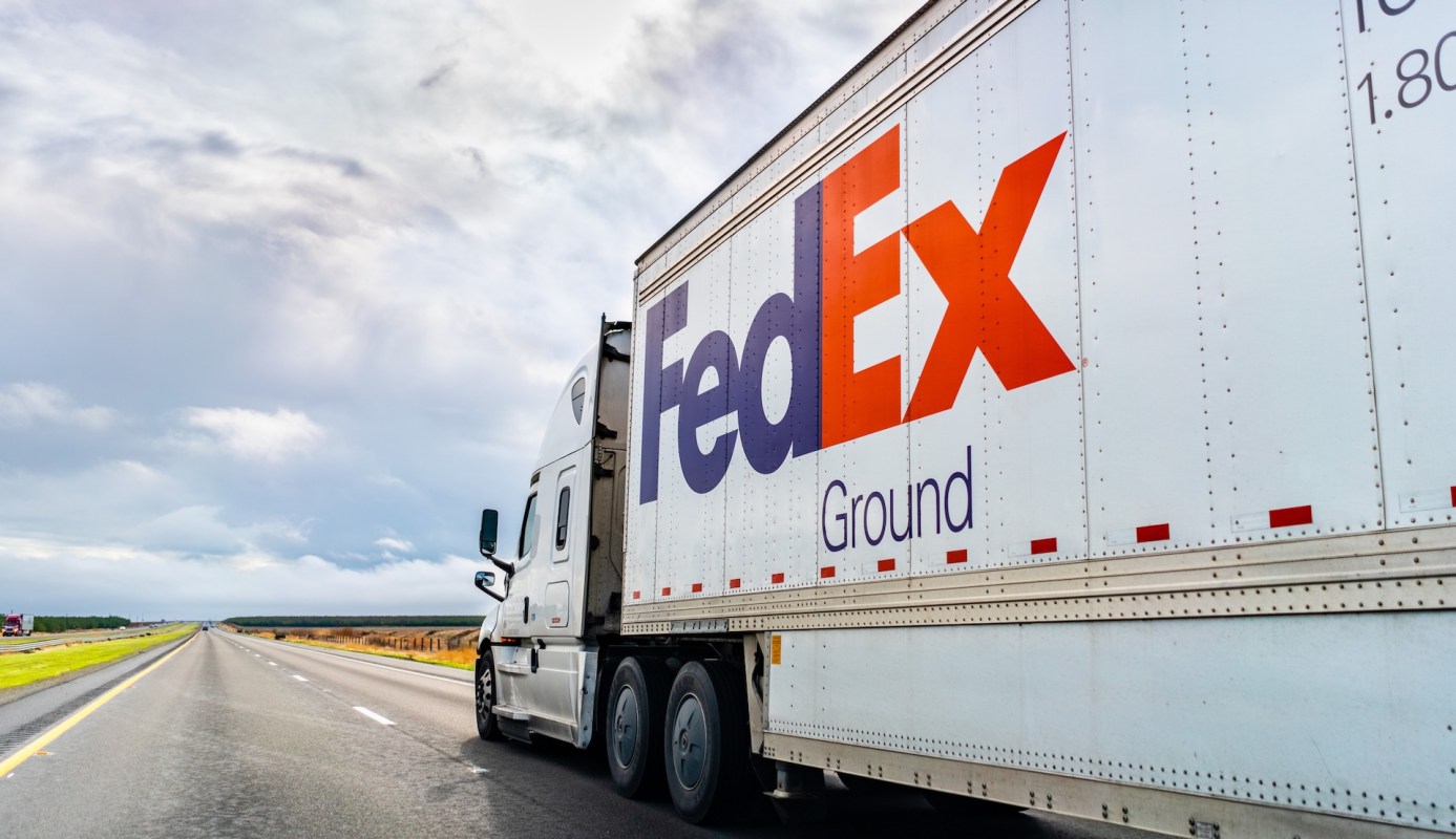 A FedEx Ground truck parked on the side of an empty highway under a cloudy sky.