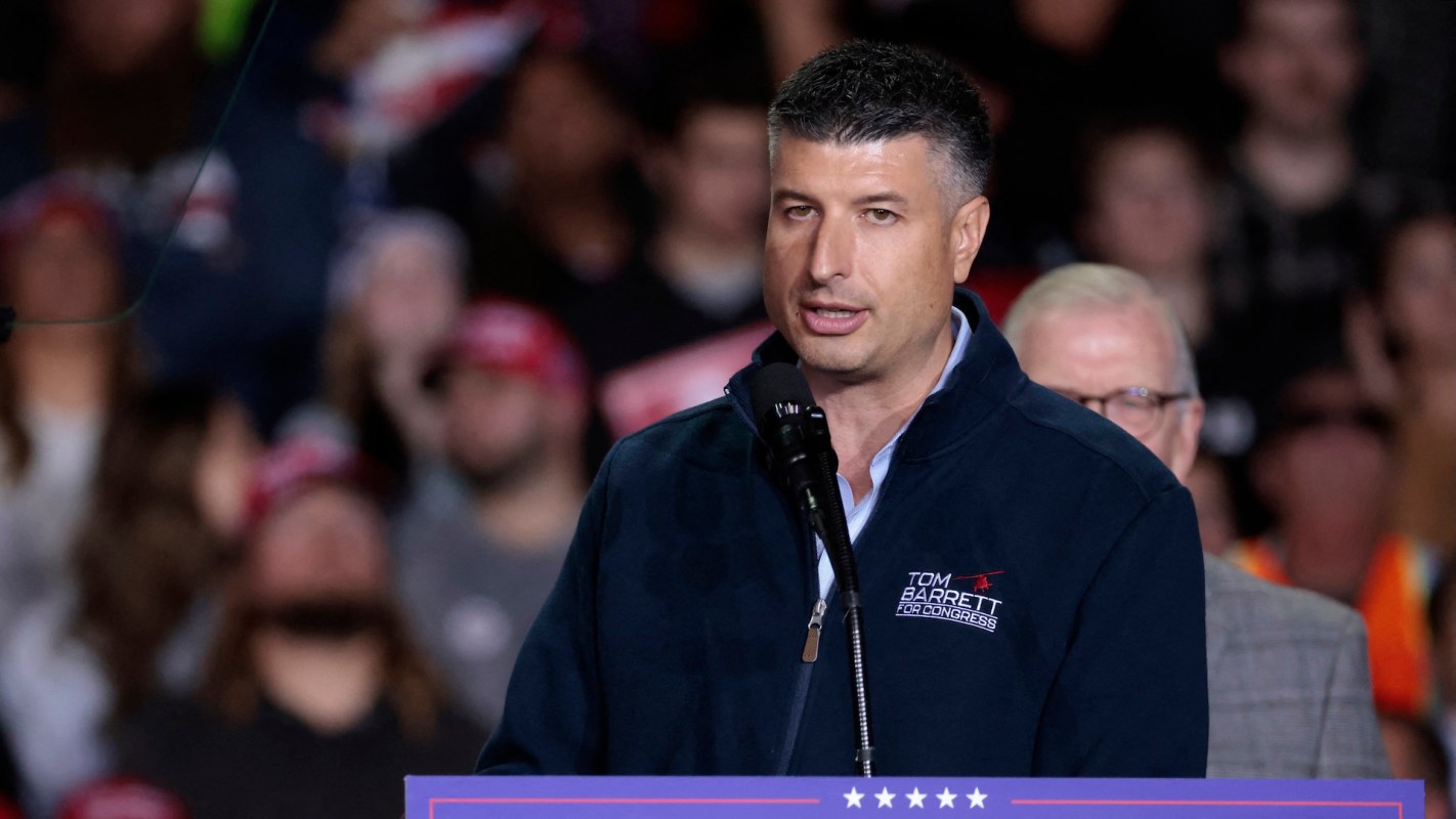 Michigan state representative Tom Barrett speaks at a podium during a political rally with a crowd in the background.