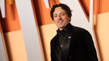 Google co-founder Sergey Brin, in a black tuxedo with a bow tie, stands against a colorful backdrop.