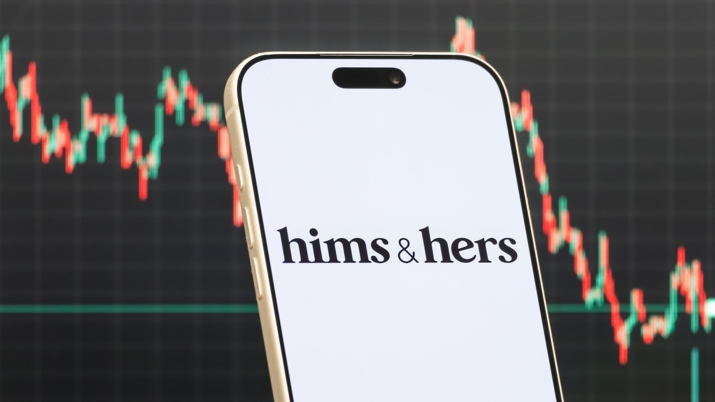 A smartphone displays the logo of "hims & hers" in front of a stock market graph.