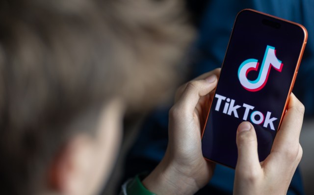 A person holding a smartphone displaying the TikTok logo.
