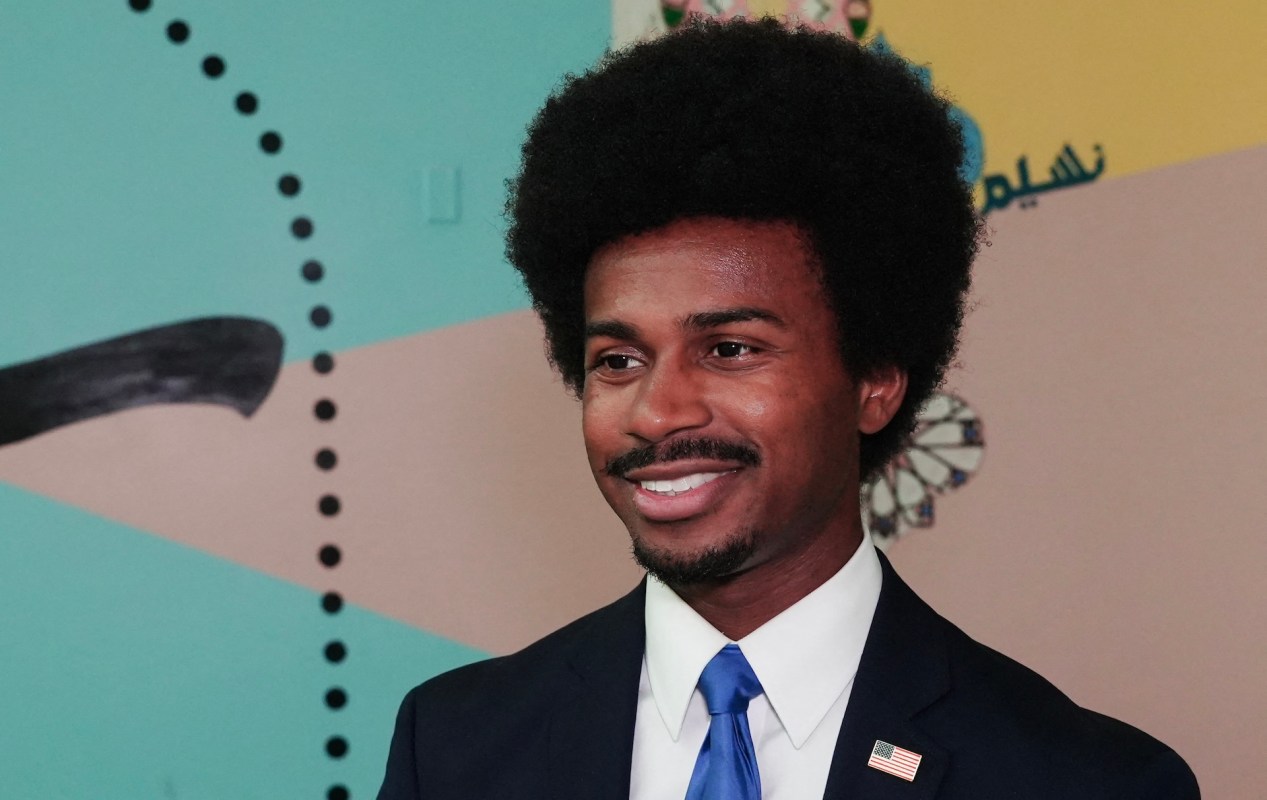 A man in a suit with a tie stands in front of a colorful mural.