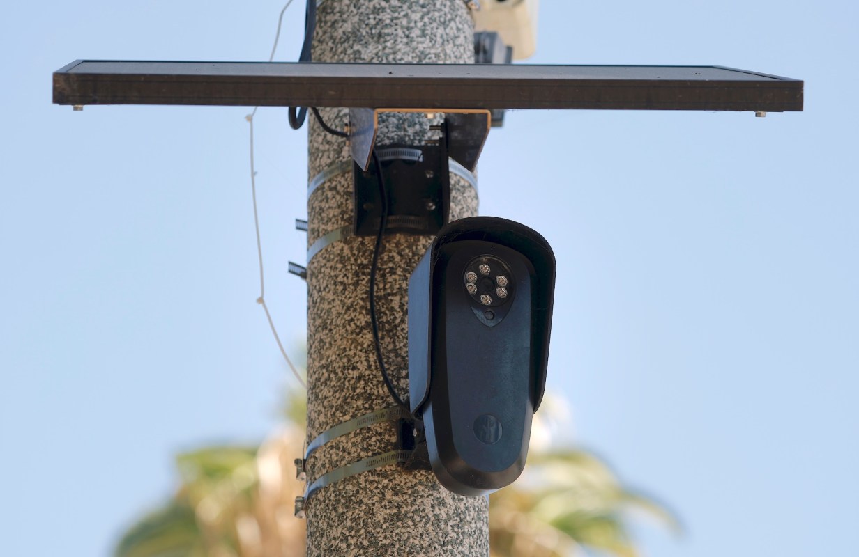 A Flock Safety surveillance camera mounted on a utility pole with a solar panel above it.