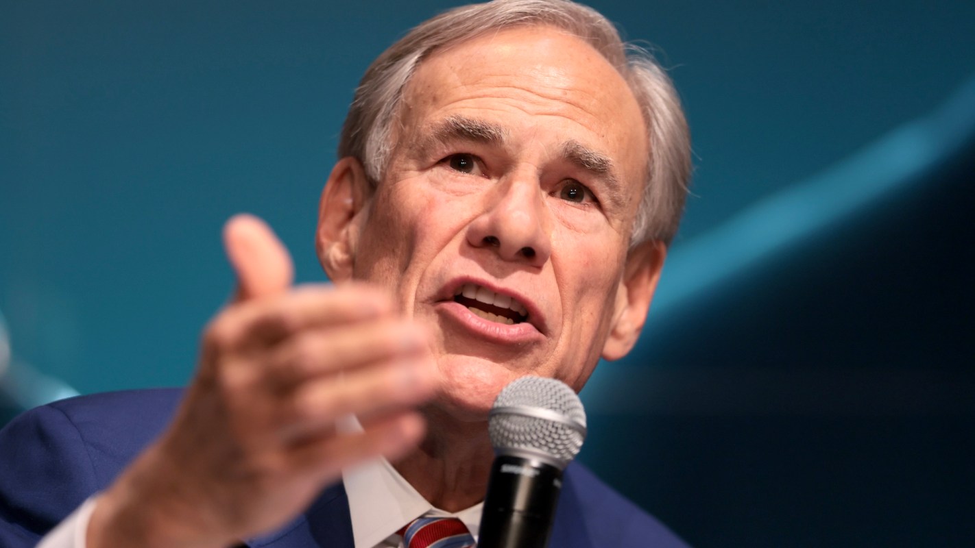 Governor Greg Abbott speaking into a microphone with his hand raised, against a blue background.