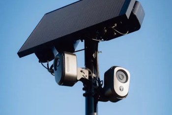 A solar panel mounted on a pole with two cameras attached below it.