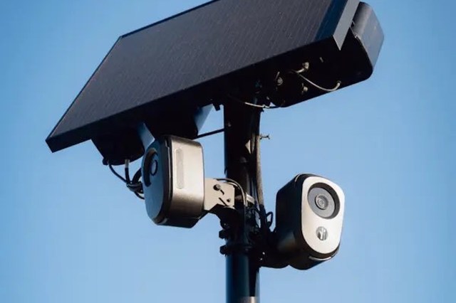 A solar panel mounted on a pole with two cameras attached below it.
