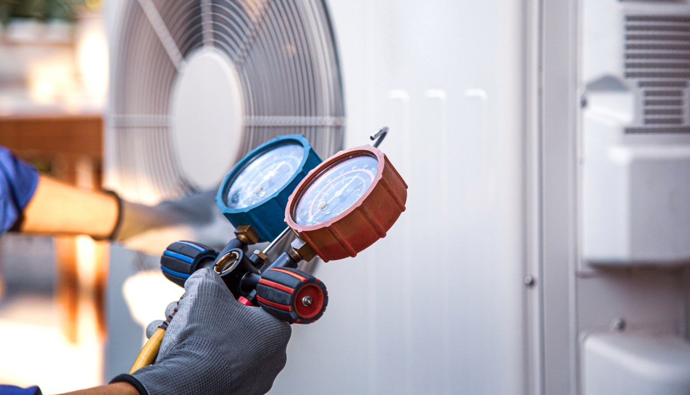 A person checking an AC unit with a gauge.