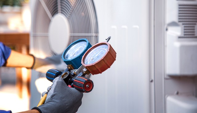 A person checking an AC unit with a gauge.