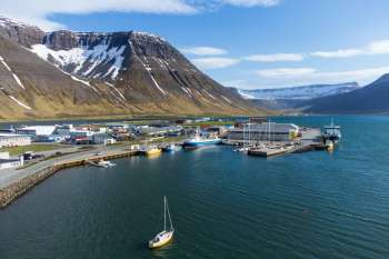 A harbor with boats and buildings, surrounded by mountains and snowy peaks.