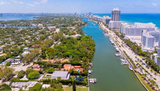 Aerial view of a waterway lined with greenery, homes, and buildings along a coastal city.