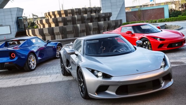 Three sports cars parked on a paved area, featuring a silver car in the foreground, a blue car in the back, and a red car on the right.