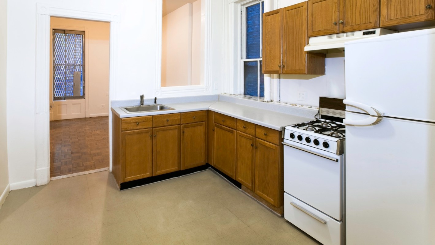 A kitchen with wooden cabinets, a stainless steel sink, a white gas stove, and a refrigerator.