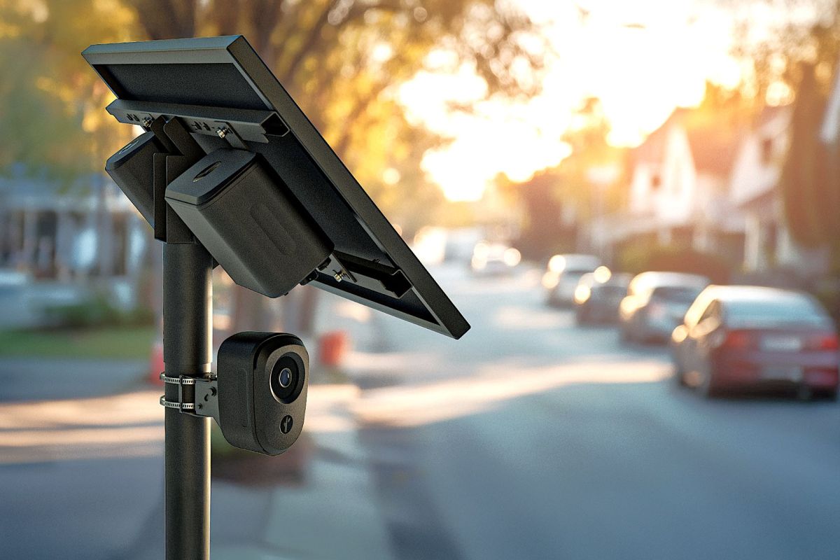 A solar panel with a camera mounted on a streetlamp on a residential street.