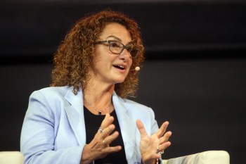 A woman speaks at a conference, gesturing with her hands in discussion.
